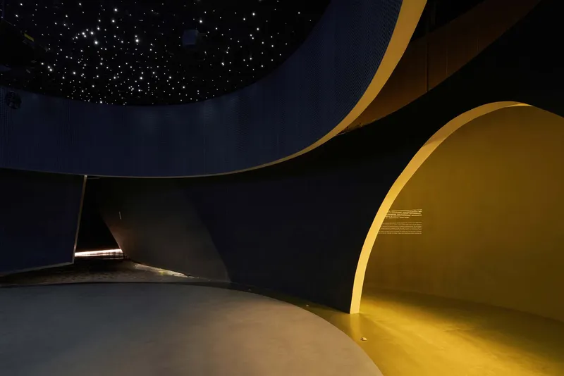 Curved interior wall with yellow illuminated alcove beneath a starlit ceiling