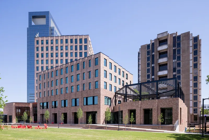 Brick podium with steel canopy structure fronting a lawn and glass tower beyond