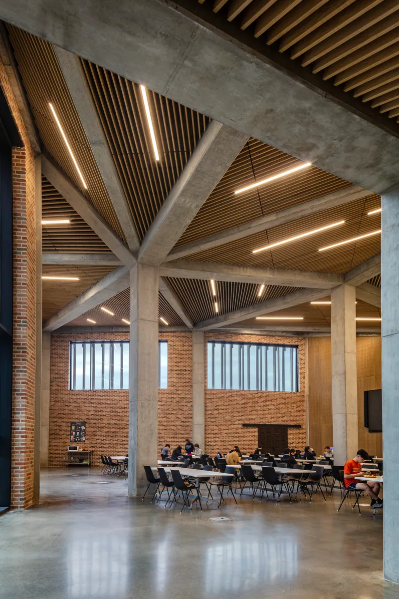 Double-height interior space with exposed concrete structure and timber-slatted ceiling panels