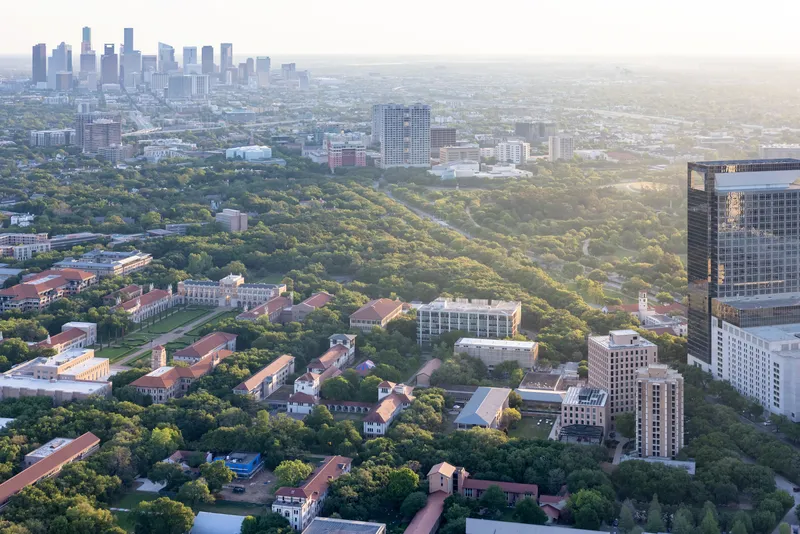 Aerial view of a campus with red-tiled roofs nestled among dense tree canopy with skyline beyond