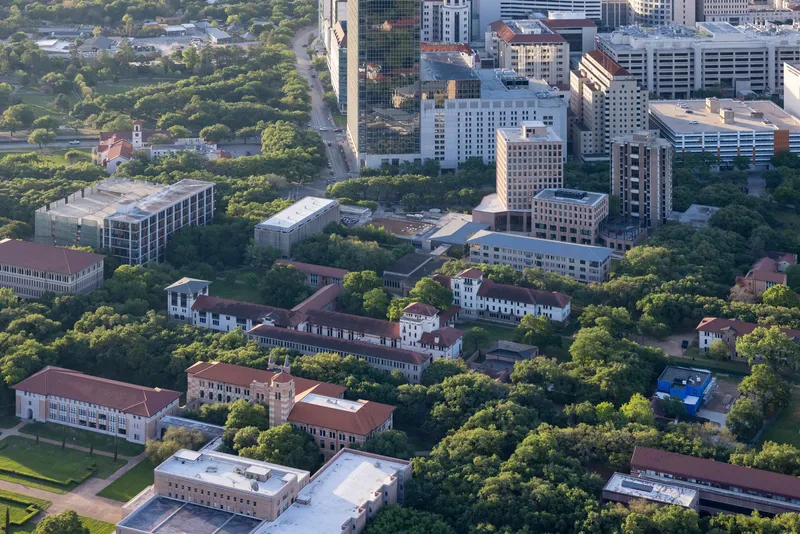 Aerial view of low-rise campus buildings with red terracotta roofs surrounded by mature trees at dusk