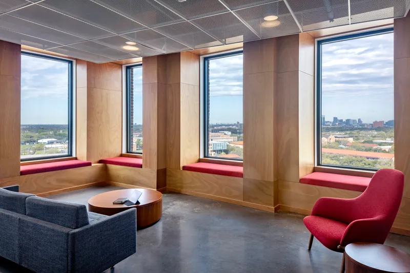Corner lounge with three tall windows framed by timber panels and built-in crimson window seats overlooking distant skyline