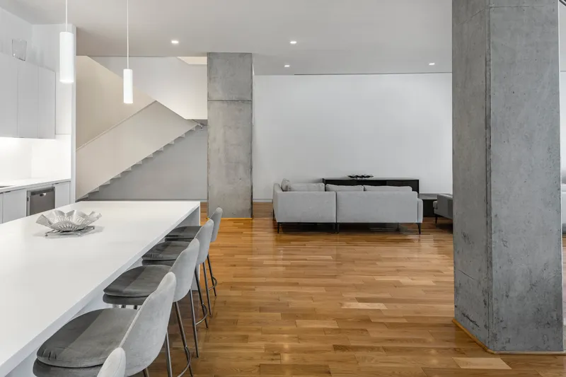 Open-plan living space with concrete columns, oak flooring, and staircase rising to upper level