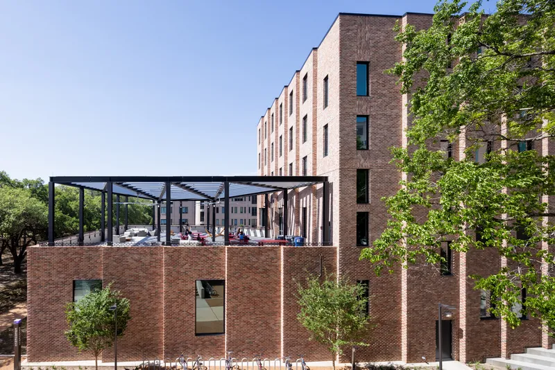 Single-story brick pavilion with steel pergola structure overlooking the courtyard with young trees in foreground