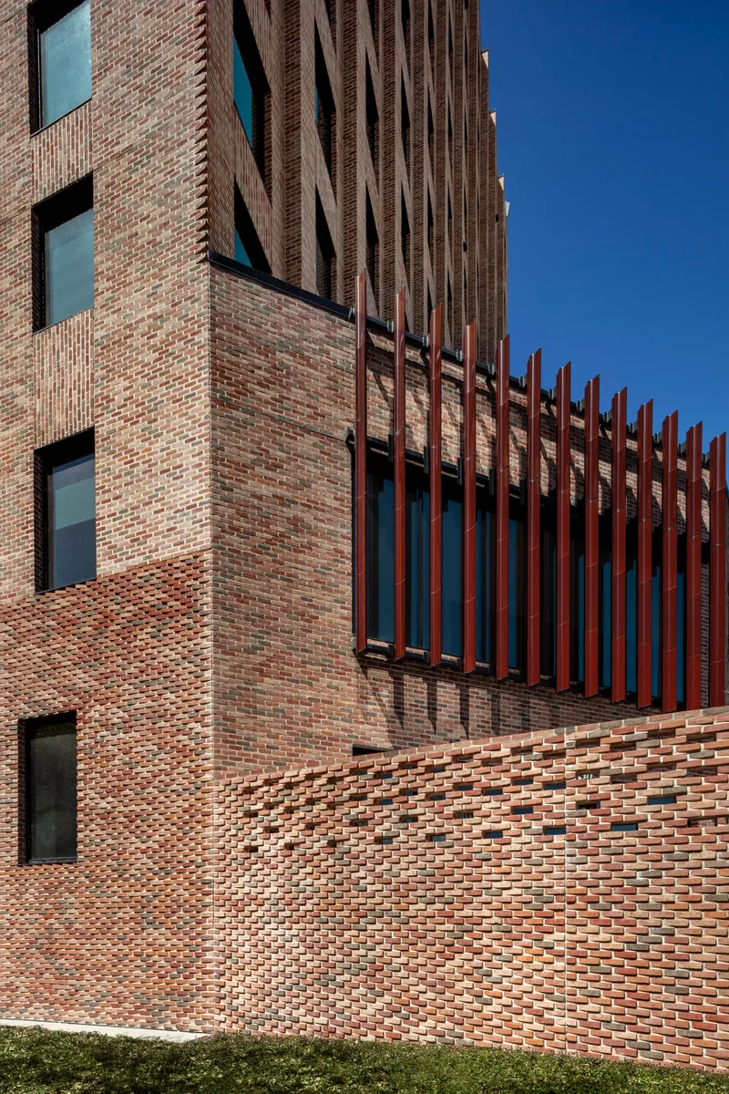 Close-up of the patterned brickwork wall meeting bronze vertical fins against a deep blue sky