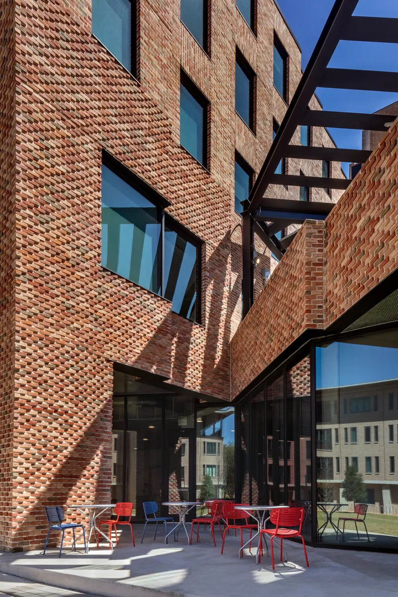 Courtyard looking up at textured brick walls with steel bridge element crossing overhead in late afternoon light