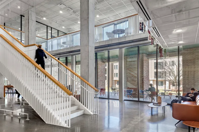 Interior view of the staircase with white vertical slats and a person ascending under exposed concrete beams
