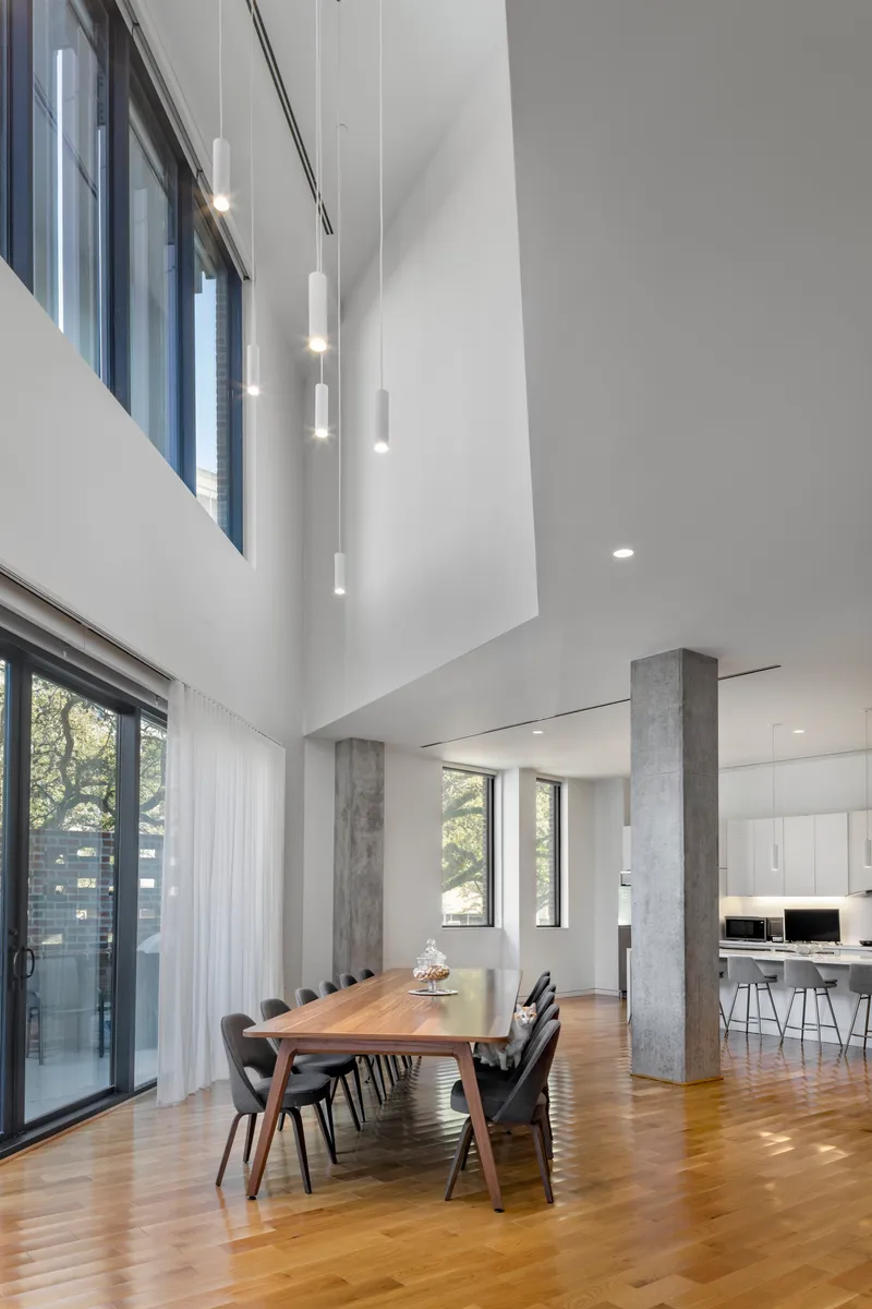 Double-height dining area with concrete columns, wood flooring, and pendant lights descending from the upper level