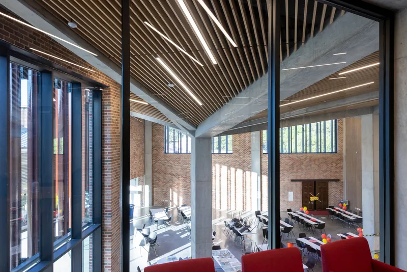 View into multi-level dining space through floor-to-ceiling glazing with exposed concrete beams and wood slat ceiling