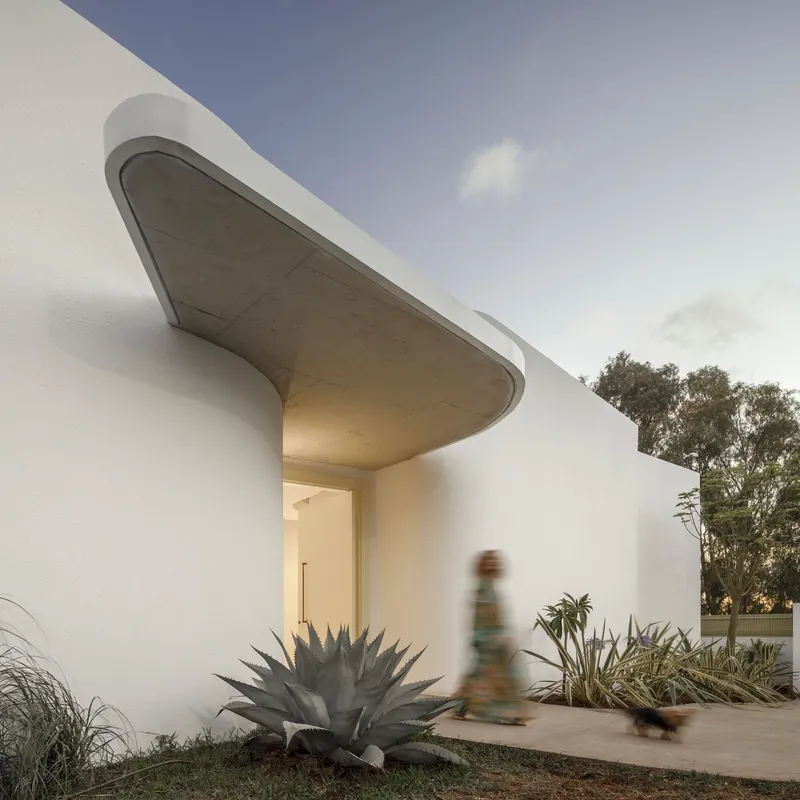 Curved concrete canopy over the entrance path with a person walking past agave plantings