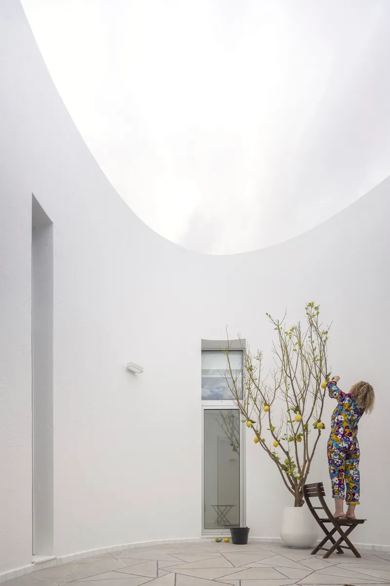 White-walled courtyard with a circular oculus overhead and a person tending to a potted tree