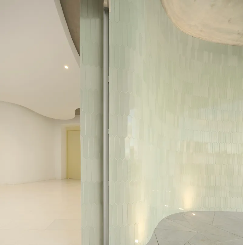 Translucent tiled partition wall separating curved interior volumes with soft natural light filtering through