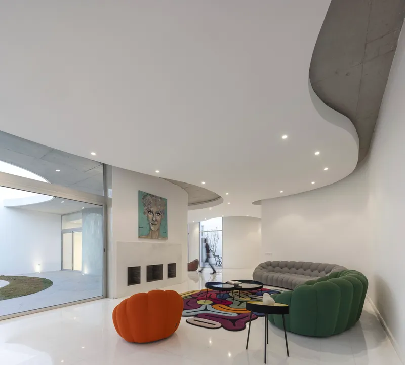 Living room with undulating ceiling cutouts revealing concrete above and colorful furniture below