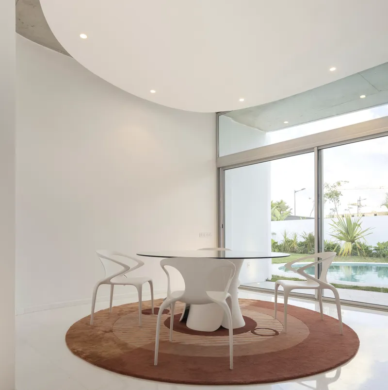 Dining area with circular table on a round rug overlooking a pool and planted courtyard