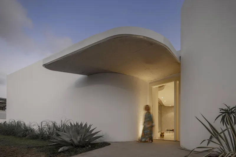 White stucco entry wall with sweeping concrete soffit and figure passing through at twilight
