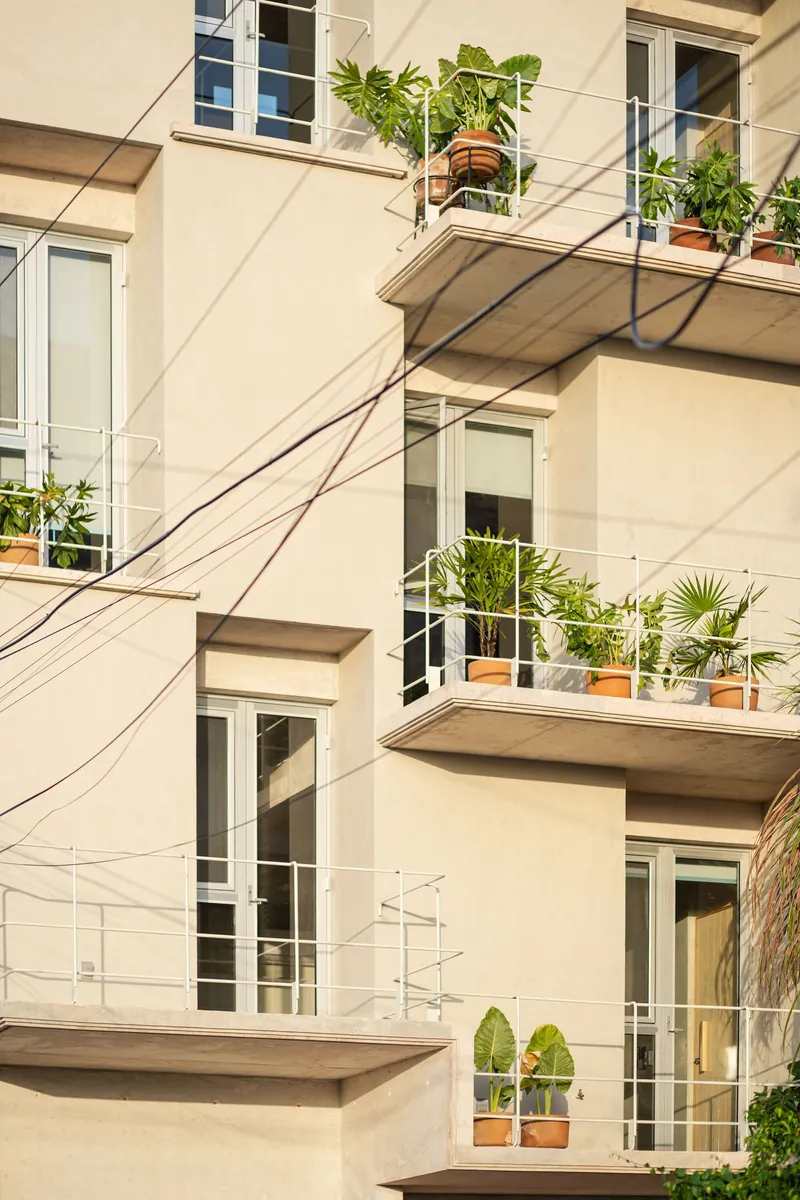 Stacked concrete balconies with potted plants and wire railings casting sharp shadows across the cream facade