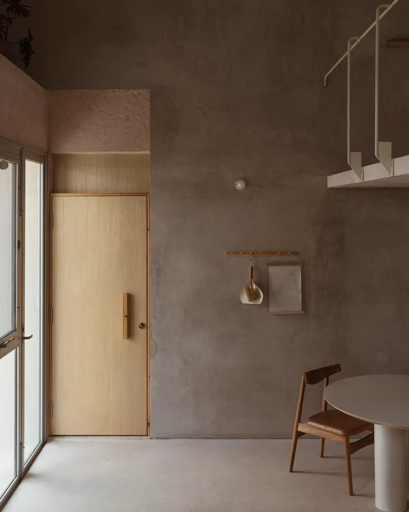Interior room with raw concrete walls, timber door, suspended brass fixtures and polished concrete floor in soft light