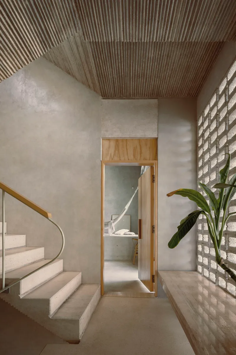 Concrete staircase with timber-framed doorway, corrugated ceiling and glass brick wall filtering daylight