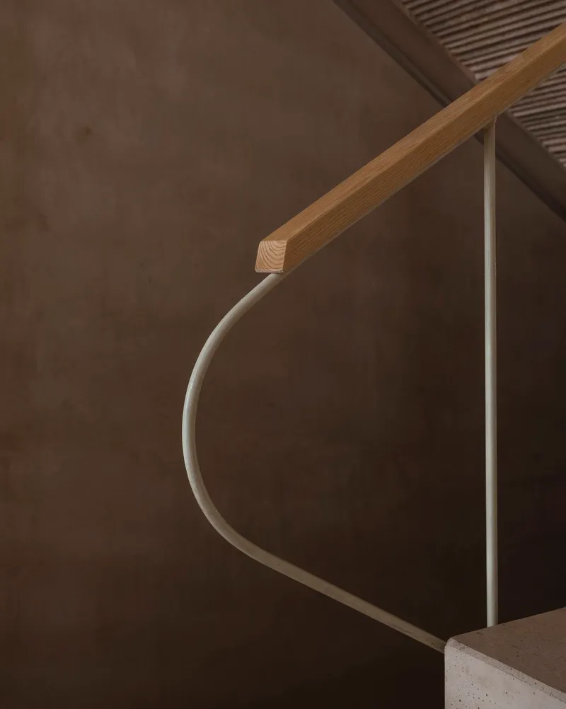 Close-up of curved timber handrail meeting a white metal railing against a concrete wall