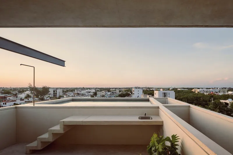 Rooftop terrace with white parapet walls, stepped seating area and low-rise neighborhood visible at dusk