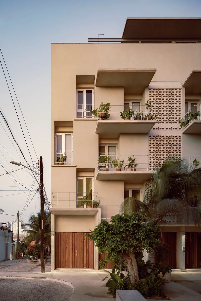 Street facade with stacked balconies, perforated brick screening, and potted plants at dusk