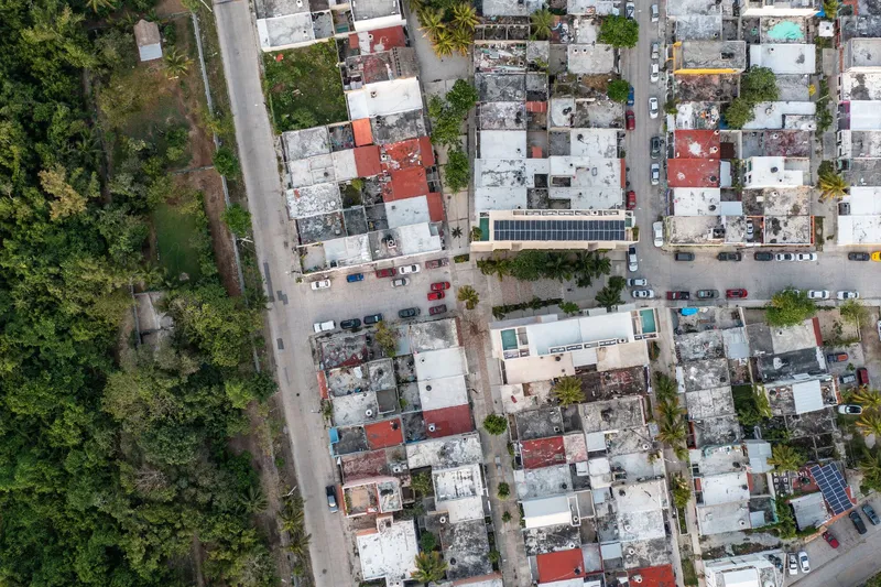 Aerial view of dense urban rooftops with mixed materials and parked vehicles lining the street