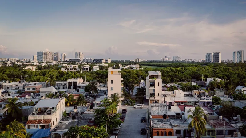 Aerial view of two white tower volumes rising above low-rise rooftops with distant high-rises on the horizon