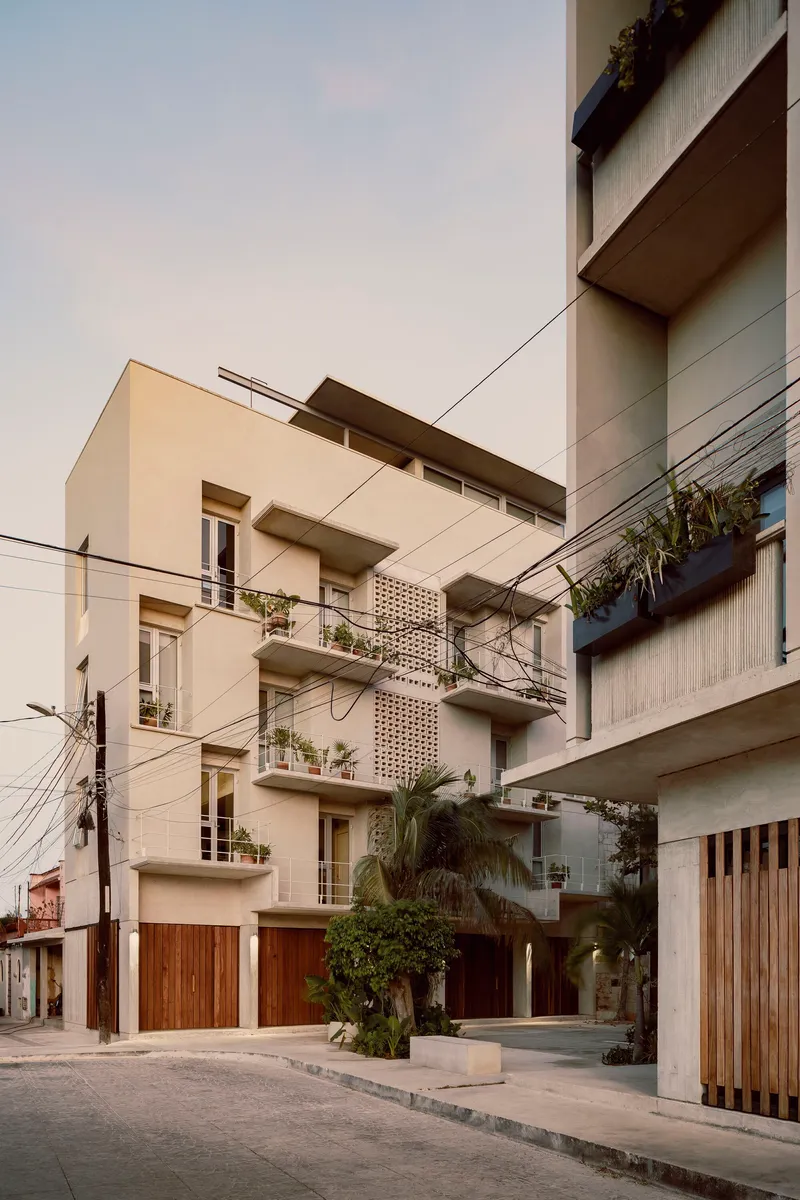 Street-level view of cream stucco facades with planted balconies and timber garage doors under overhead power lines
