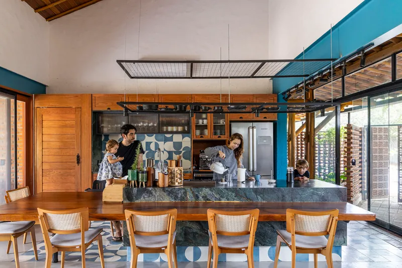 Kitchen island with dark stone countertop facing caned dining chairs under an exposed timber ceiling