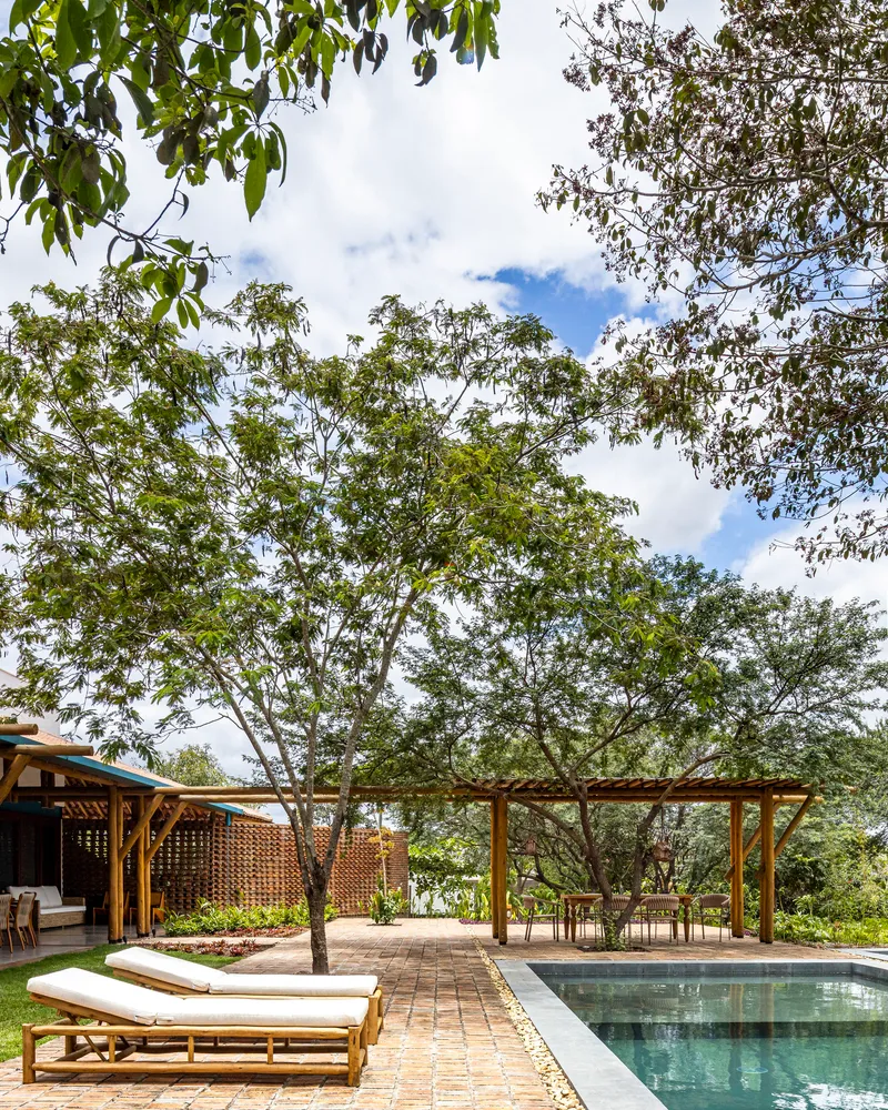 Pool deck with brick pavers and wooden loungers framed by mature trees and lattice screening