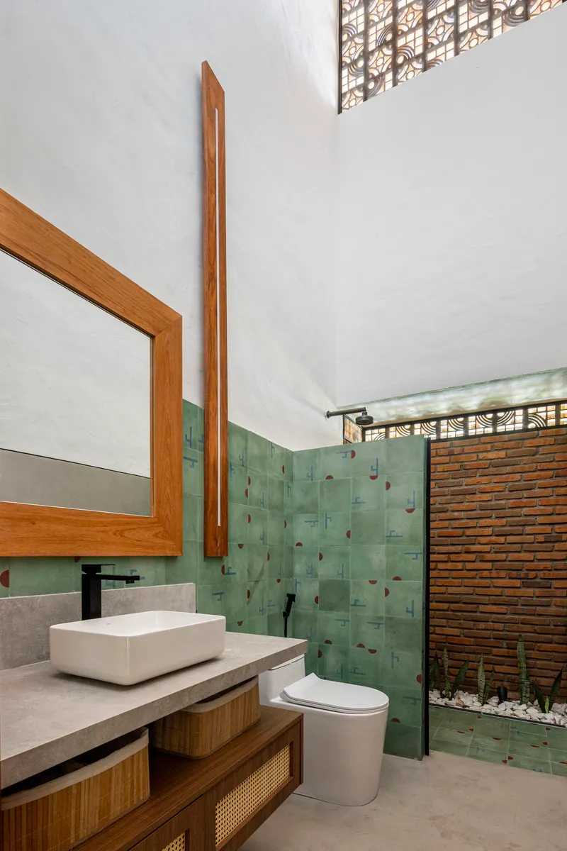 Bathroom with green tile accent wall, timber-framed mirror, and glass shower screen opening to courtyard