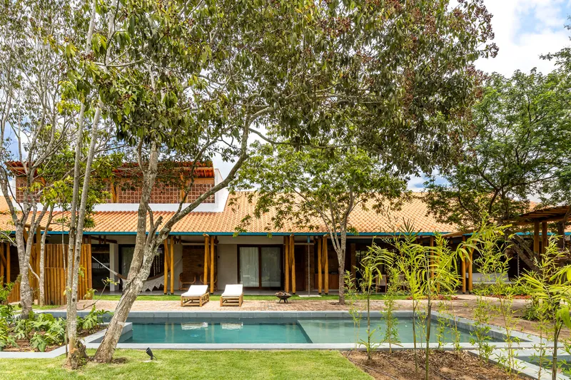 Rear facade with timber columns and tile roof overlooking a swimming pool framed by mature trees