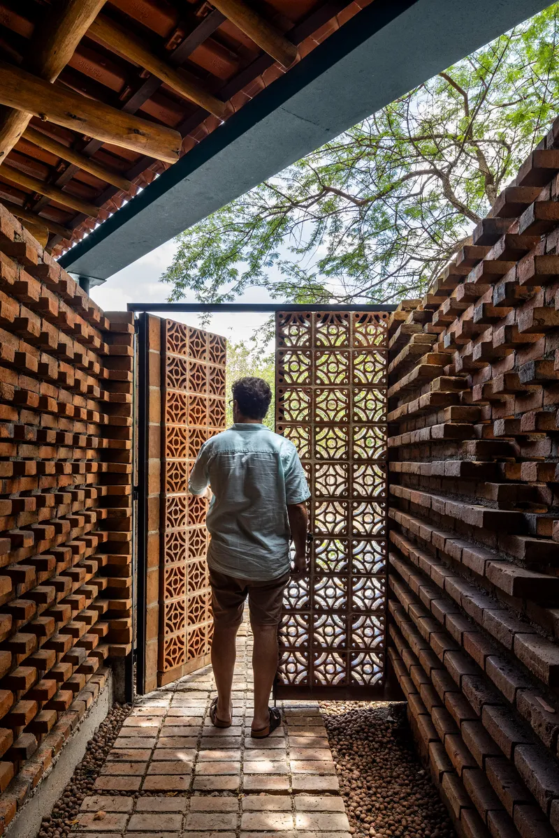 Person walking through brick-lined corridor toward patterned metal gate under a timber overhang
