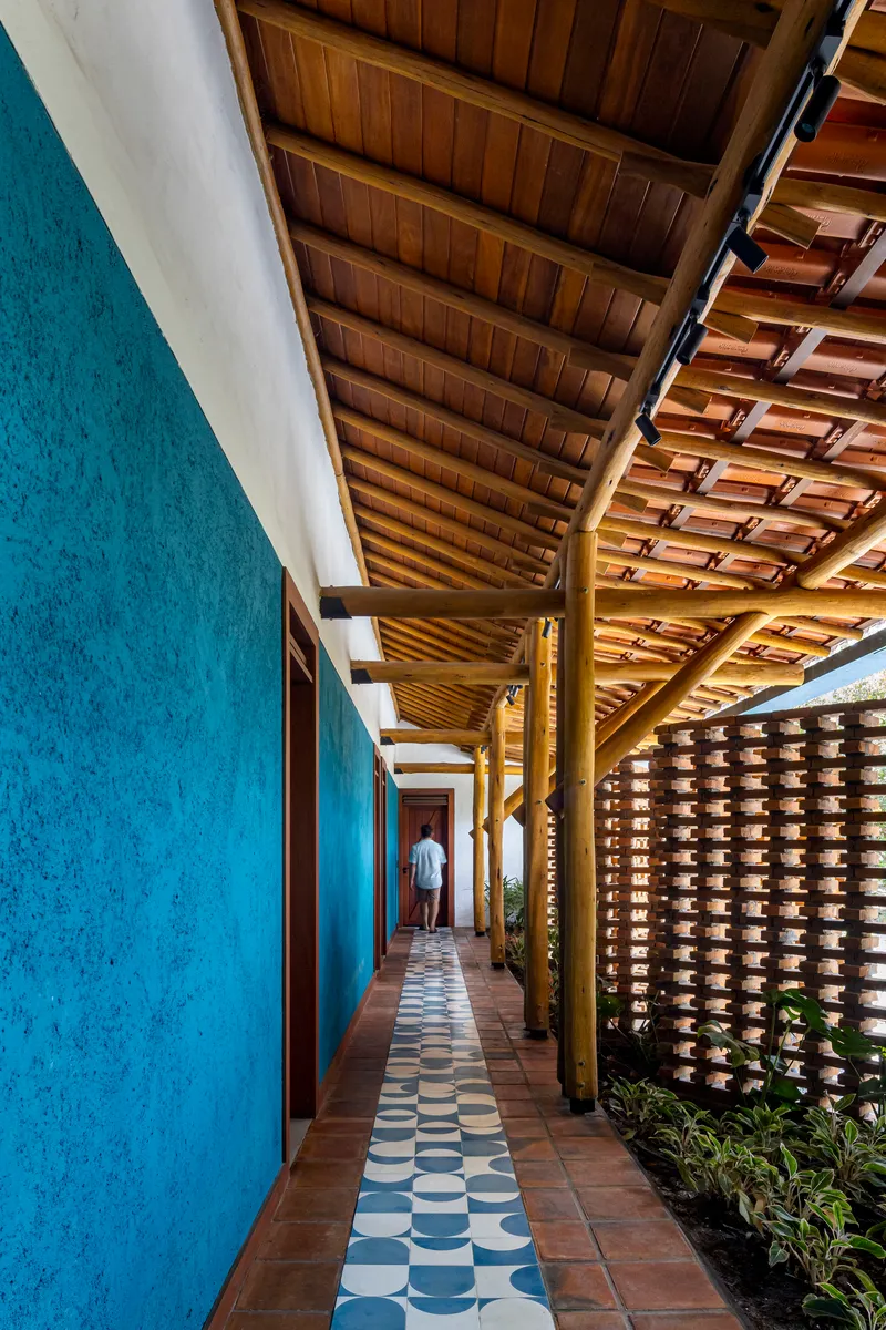 Covered walkway with blue plaster wall, patterned tile floor and perforated brick screen with plantings