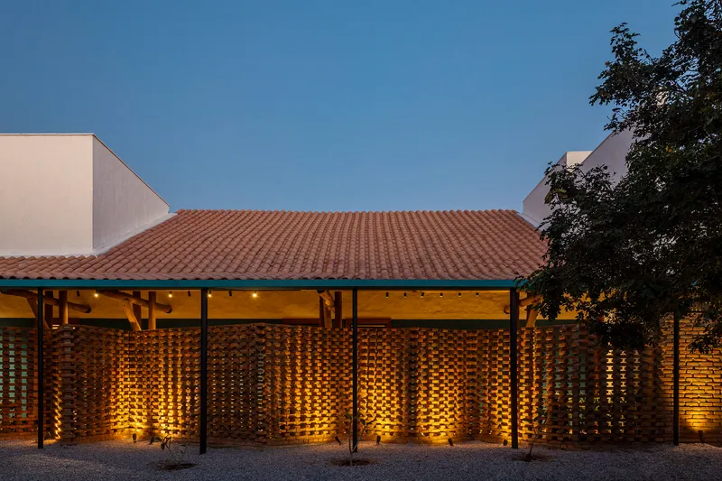 Clay tile roof and illuminated perforated brick screen facade beneath timber eaves at twilight