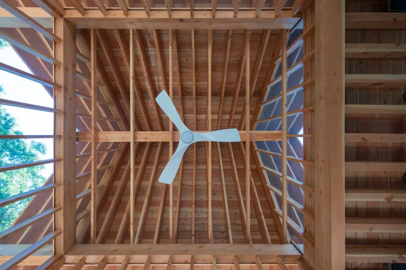 Looking up into exposed timber roof framing with ceiling fan and clerestory windows