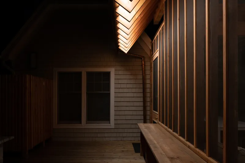 Nighttime view of the timber deck with illuminated vertical slat screen and exposed roof rafters