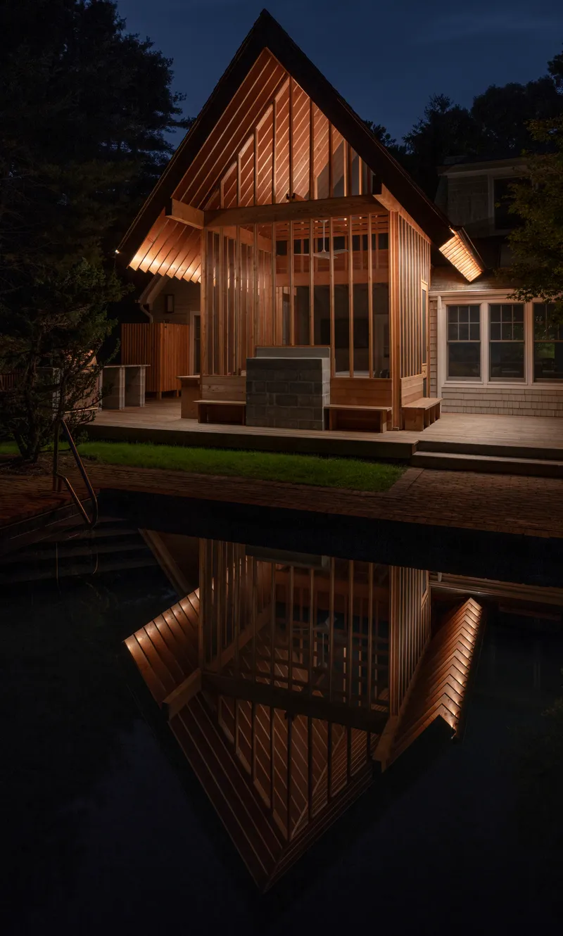 Poolside pavilion with gabled roof and vertical timber cladding reflected in still water at twilight