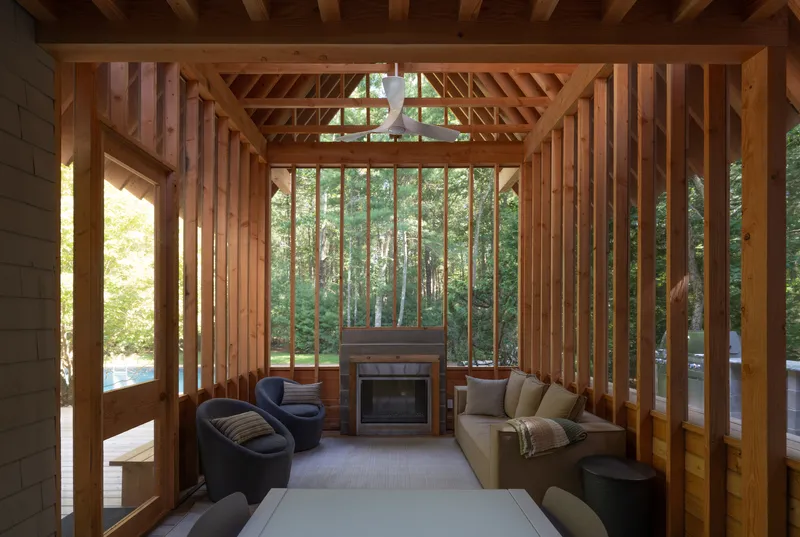 Interior of the timber frame pavilion showing exposed rafters, vertical slats and fireplace with forest view