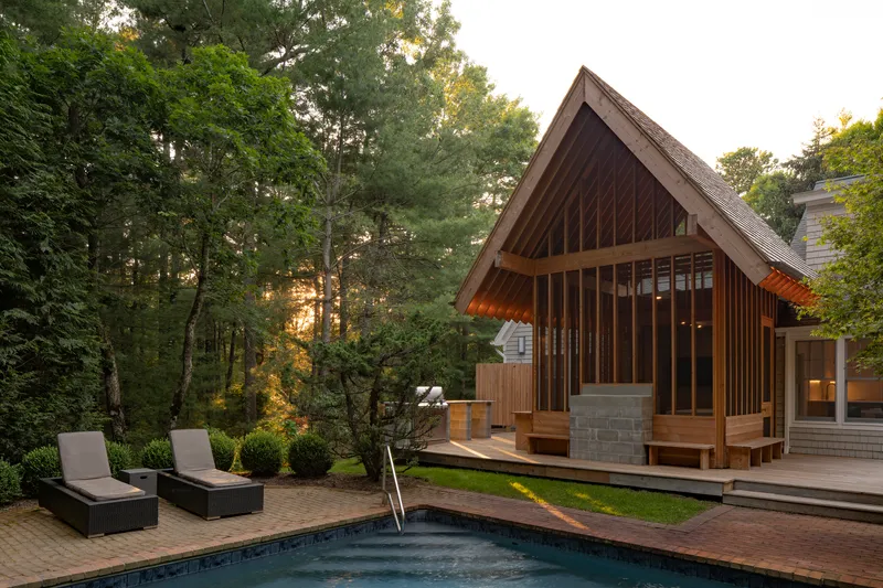 Poolside view of the timber pavilion with concrete block base and surrounding forest at sunset