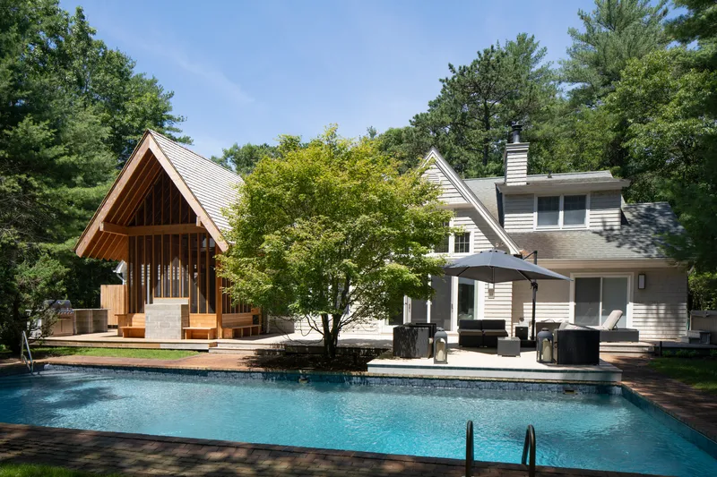 Pool terrace with open-air pavilion and white clapboard residence framed by mature trees