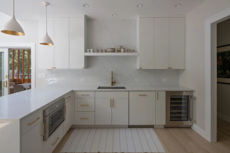 White kitchen with marble backsplash, brass hardware, and light wood flooring