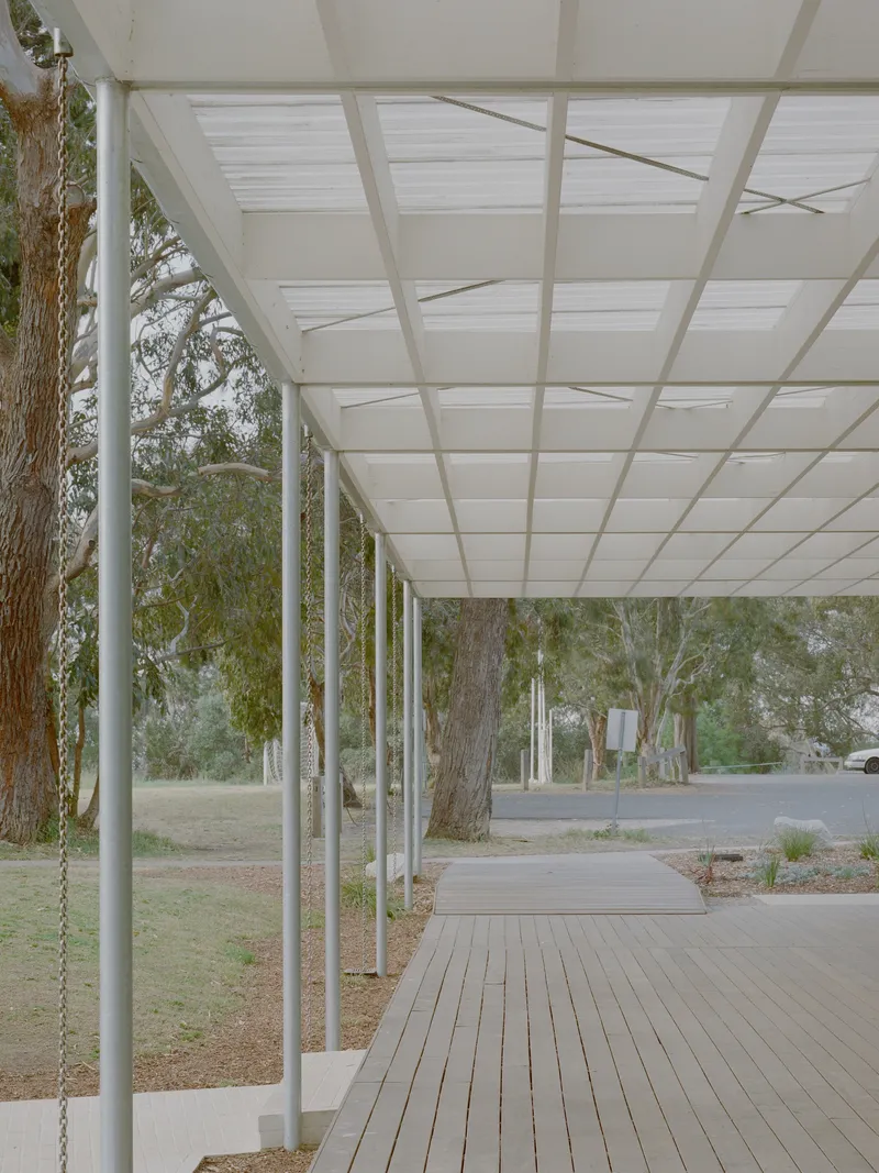 Detail of steel columns supporting translucent paneled canopy along timber boardwalk with eucalyptus trunks visible