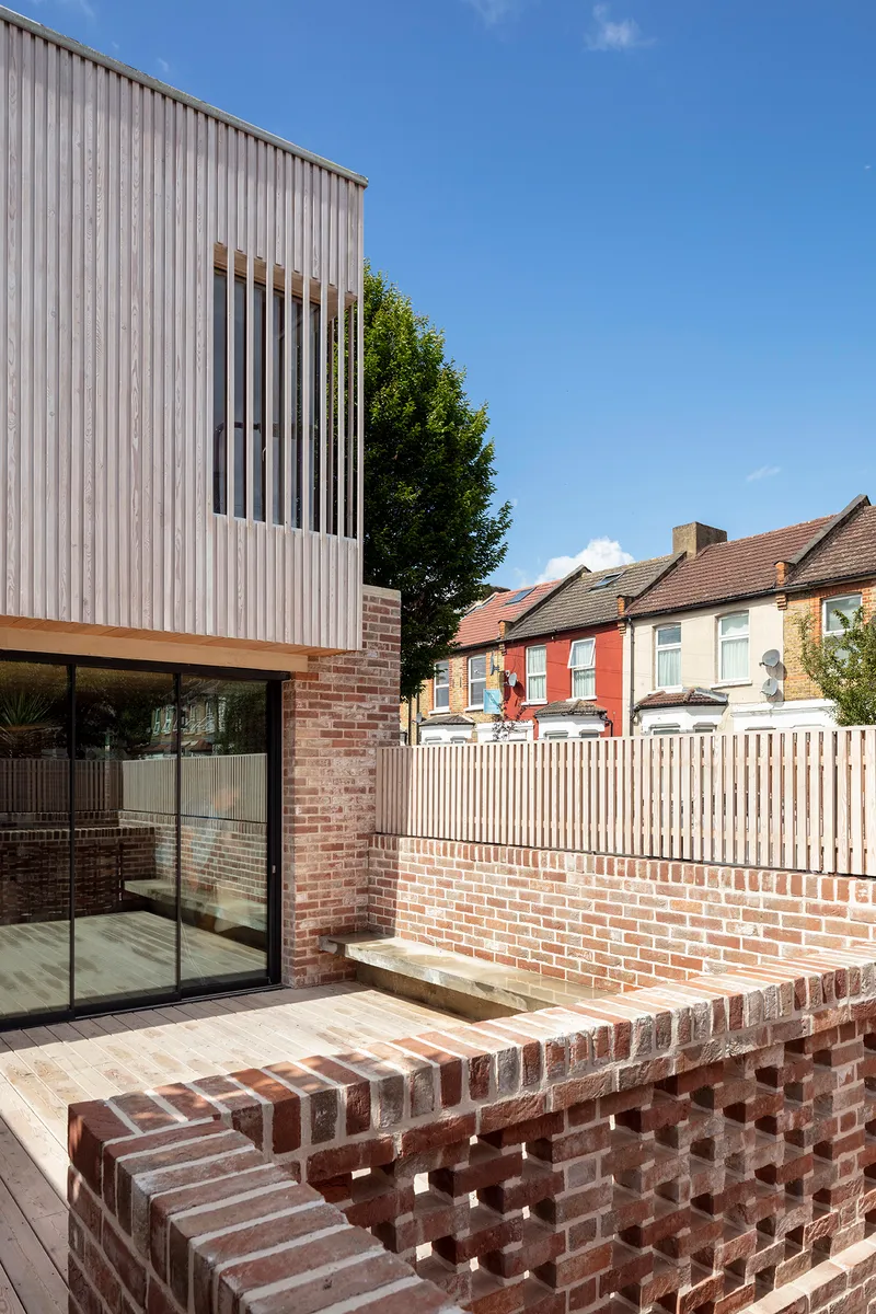 Timber deck terrace with perforated brick seating wall alongside painted stripe fence and neighboring houses
