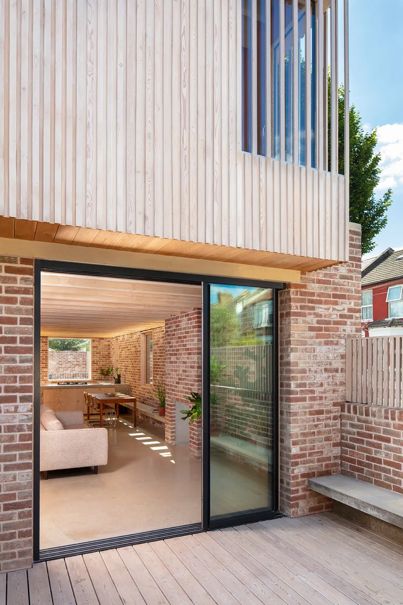 Sliding glass door opening from timber deck into living space with exposed brick walls and timber soffit