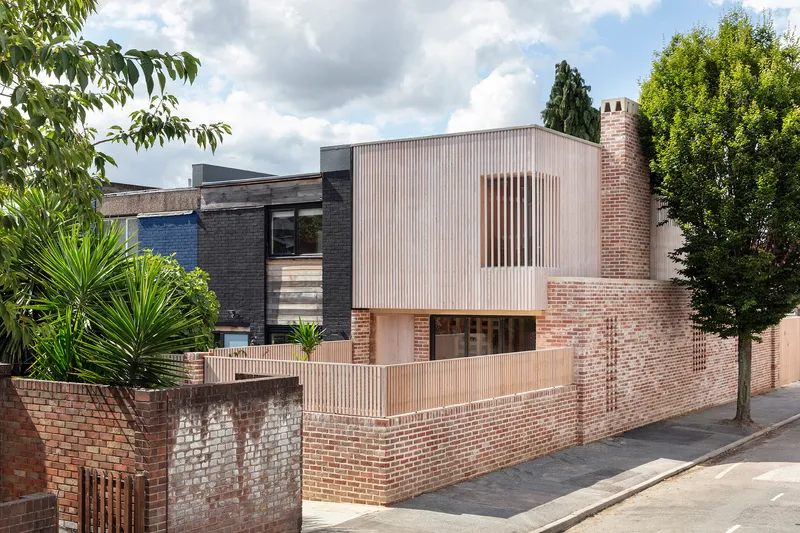 Facade showing corrugated metal upper story above perforated brick walls with timber fencing and street trees