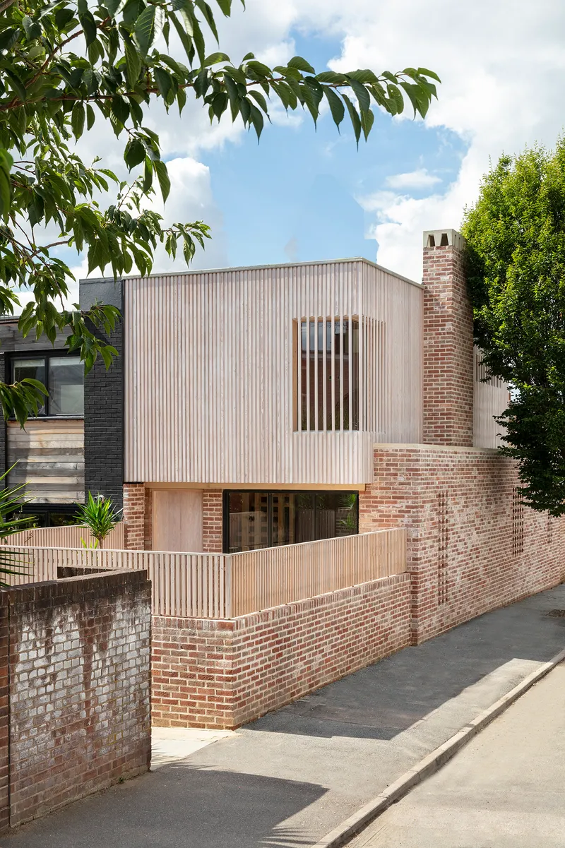 Street elevation showing corrugated metal volume with vertical slot window above perforated brick base and timber screening