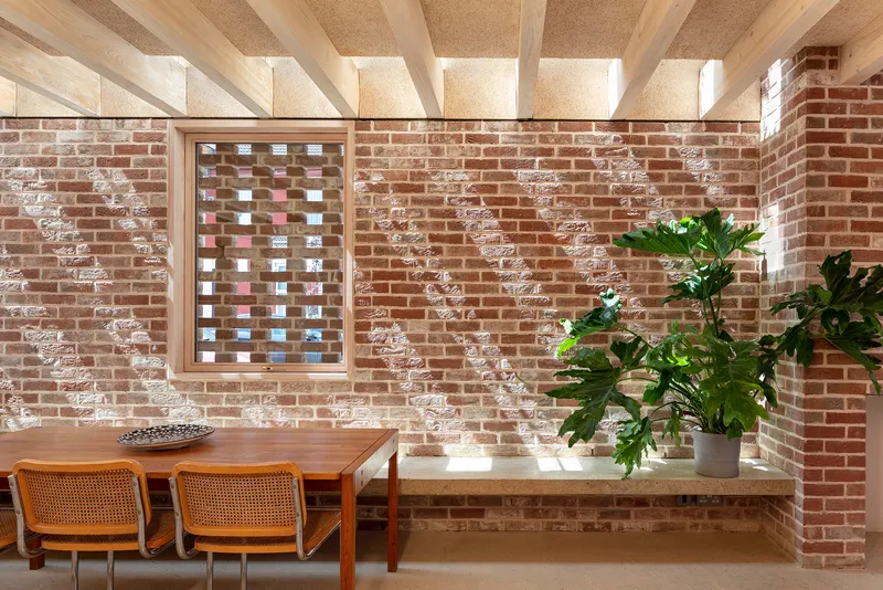 Interior dining area with exposed brick walls, timber ceiling beams and potted plants on a built-in concrete bench