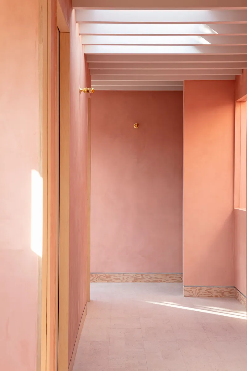 Doorway sequence through pink plastered rooms with plywood baseboards and overhead skylight slots