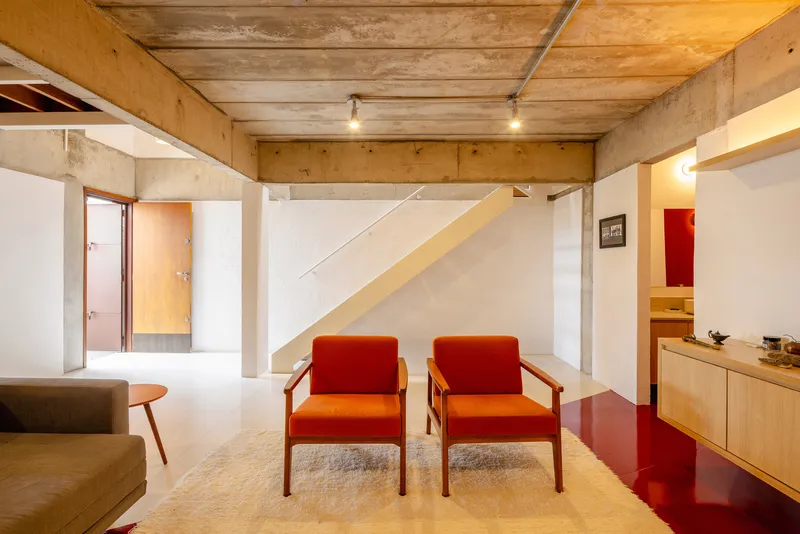 Double-height living room with exposed concrete ceiling beams and plywood walls above white volumes